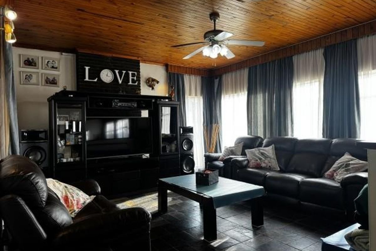 A spacious living room featuring a warm timber tongue and groove ceiling, ceiling fan, tiled flooring, and integrated media cabinetry.