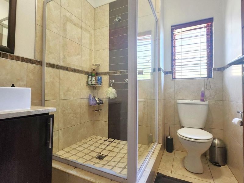 A functional bathroom featuring a glass-enclosed shower, a modern vanity with a basin, and a toilet, finished with neutral wall and floor tiling.
