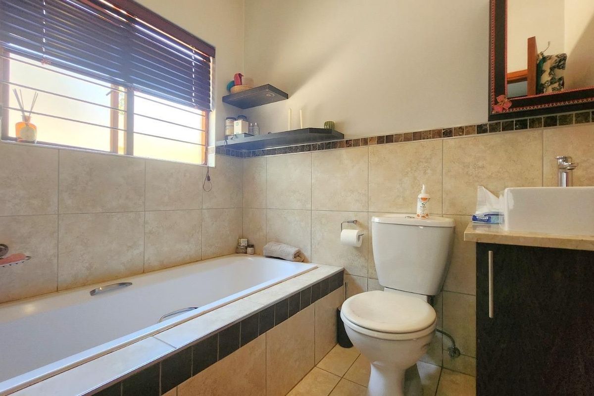 A functional bathroom featuring a built-in bathtub, a modern vessel sink on a vanity cabinet, and neutral wall tiling with decorative accents.
