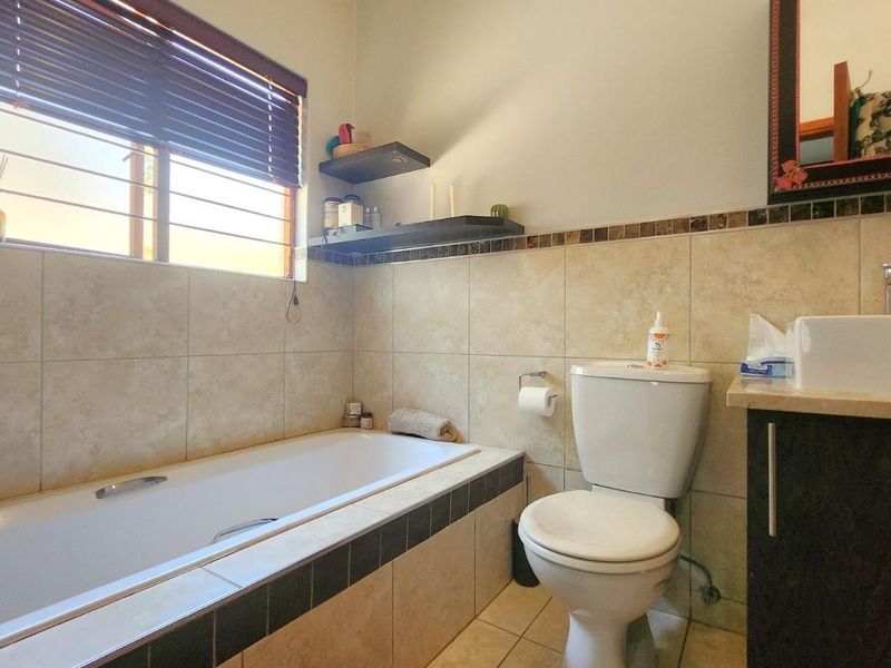 A functional bathroom featuring a built-in bathtub, a modern vessel sink on a vanity cabinet, and neutral wall tiling with decorative accents.