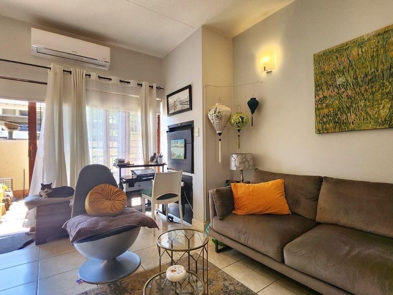 A comfortable living room featuring tiled flooring, a wall-mounted air conditioning unit, and a sliding glass door providing access to an outdoor patio area.