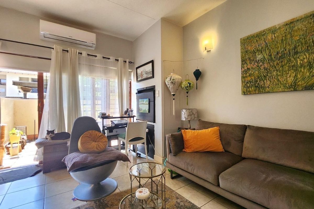 A comfortable living room featuring tiled flooring, a wall-mounted air conditioning unit, and a sliding glass door providing access to an outdoor patio area.