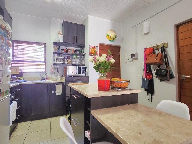 A functional kitchen featuring dark cabinetry, laminate countertops, a central island, and tiled flooring, providing a practical workspace for daily meal preparation.