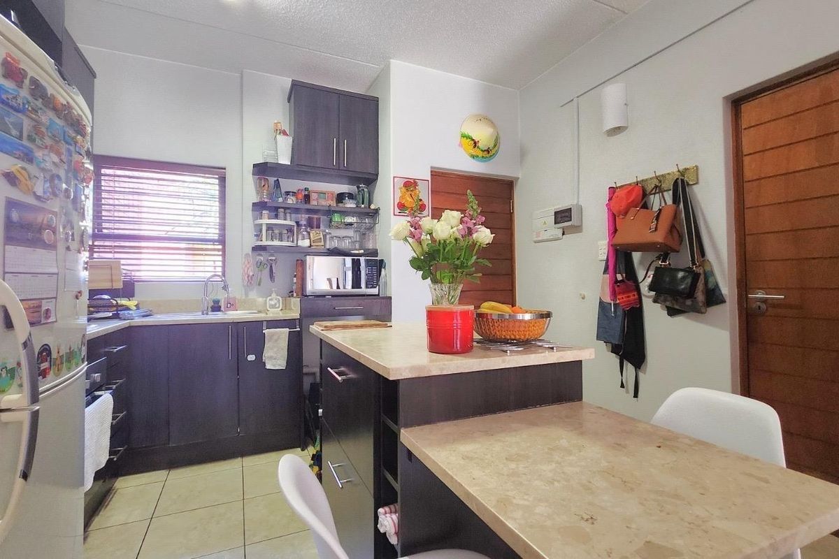 A functional kitchen featuring dark cabinetry, laminate countertops, a central island, and tiled flooring, providing a practical workspace for daily meal preparation.