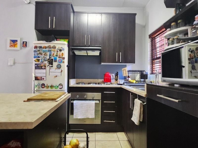 A functional kitchen featuring dark wood cabinetry, laminate countertops, built-in oven, gas hob, and tiled flooring, offering a practical layout for daily cooking.