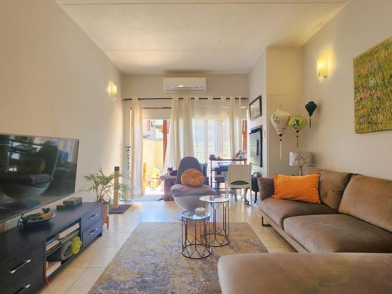 A comfortable living room featuring tiled flooring, a wall-mounted air conditioning unit, and direct access to an outdoor patio area through sliding glass doors.