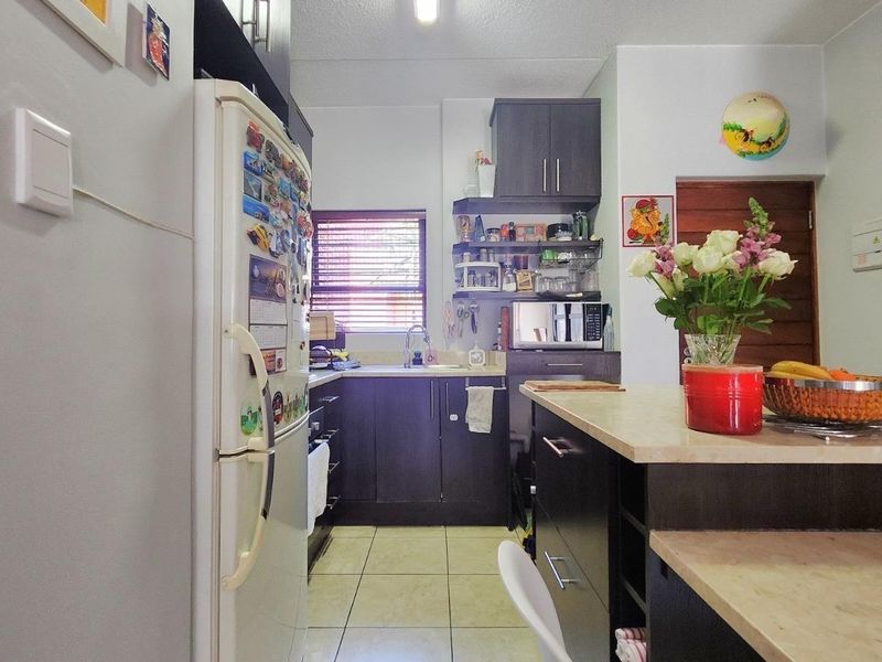 A functional kitchen featuring dark cabinetry, laminate countertops, a central island, and tiled flooring, providing a practical workspace for daily meal preparation.