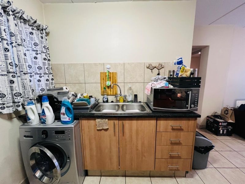 A functional kitchen area featuring laminate cabinetry, a double bowl stainless steel sink, tiled backsplash, and space for a washing machine.