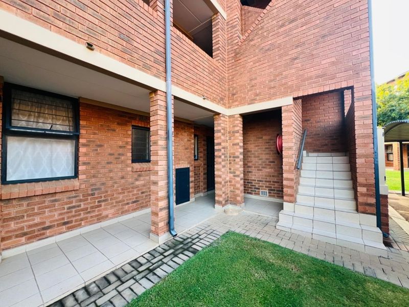 A view of the apartment building exterior featuring face brick construction, a tiled patio area, and a concrete staircase leading to upper levels.