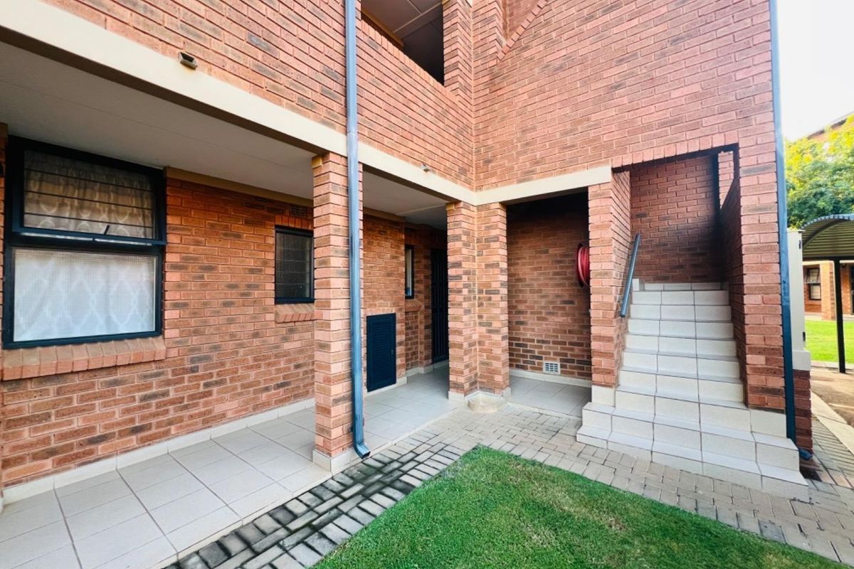 A view of the apartment building exterior featuring face brick construction, a tiled patio area, and a concrete staircase leading to upper levels.