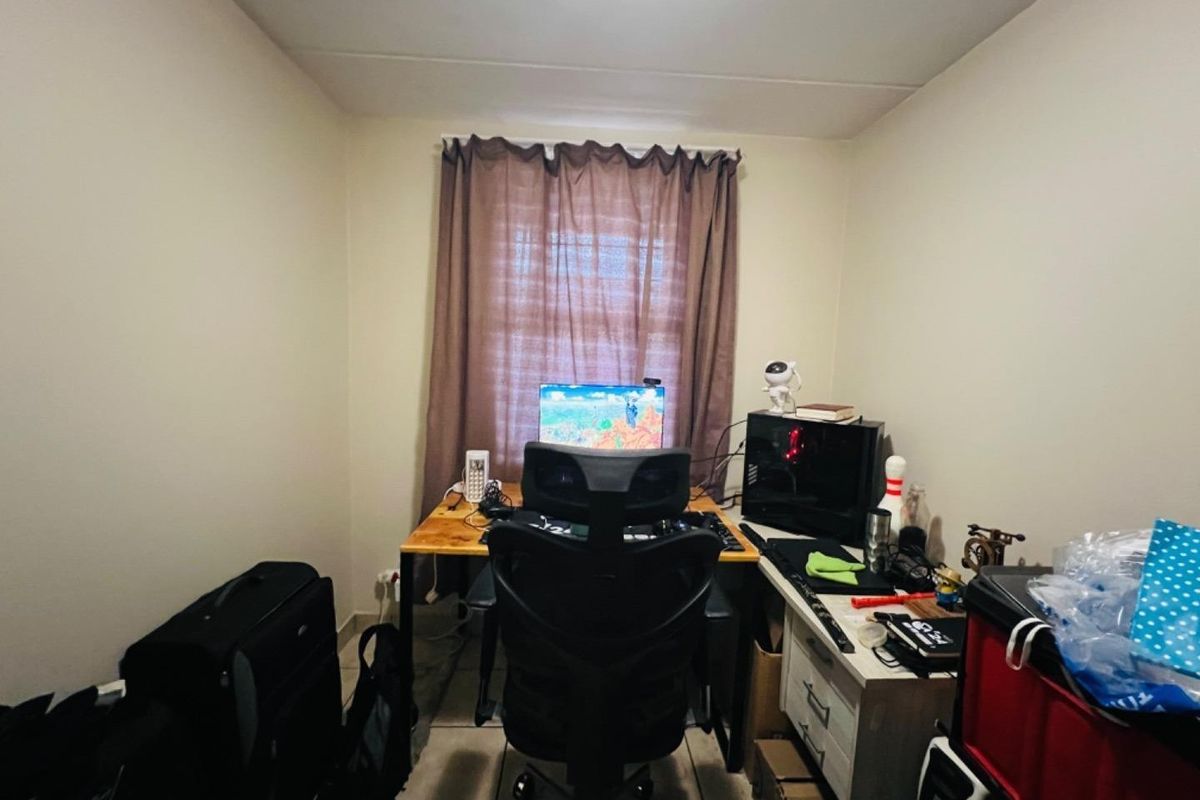 A small bedroom or study area featuring tiled flooring and a single window, currently utilized as a home office space.