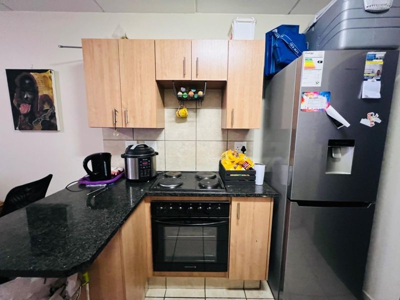 Compact kitchen featuring light wood laminate cabinetry, dark granite countertops, a tiled backsplash, and a built-in electric oven with hob.
