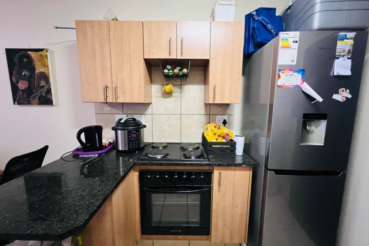 Compact kitchen featuring light wood laminate cabinetry, dark granite countertops, a tiled backsplash, and a built-in electric oven with hob.