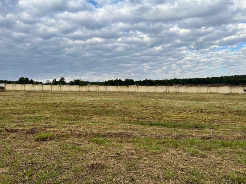 A view of a vacant residential plot featuring a long perimeter wall with security wire, set against a cloudy sky.