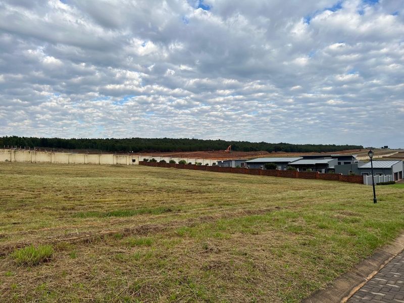 A vacant residential plot featuring a perimeter wall, paved verge, and street light, situated in a developing estate with surrounding landscape views.