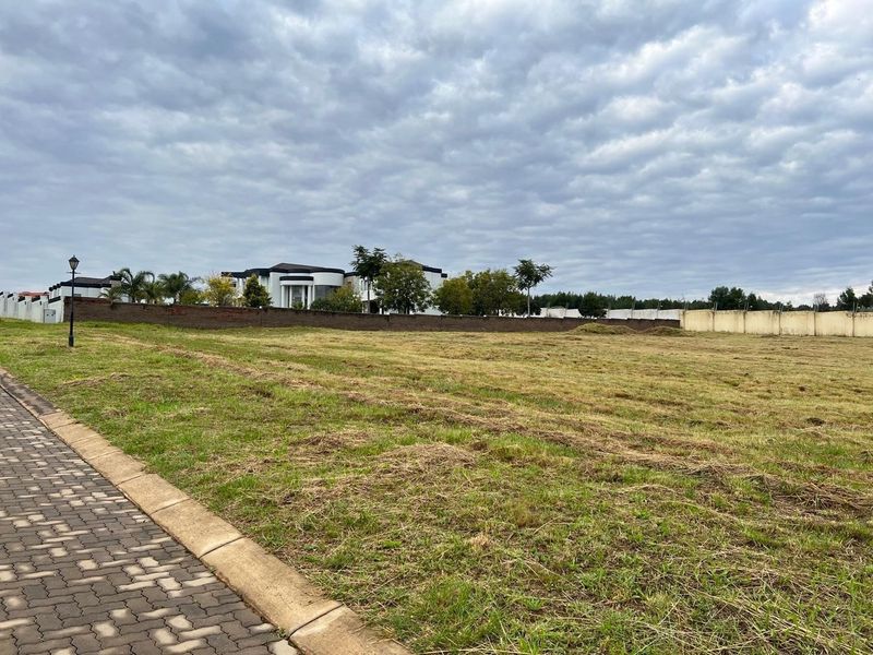 A vacant residential plot featuring a paved sidewalk, perimeter walling, and established neighborhood surroundings.