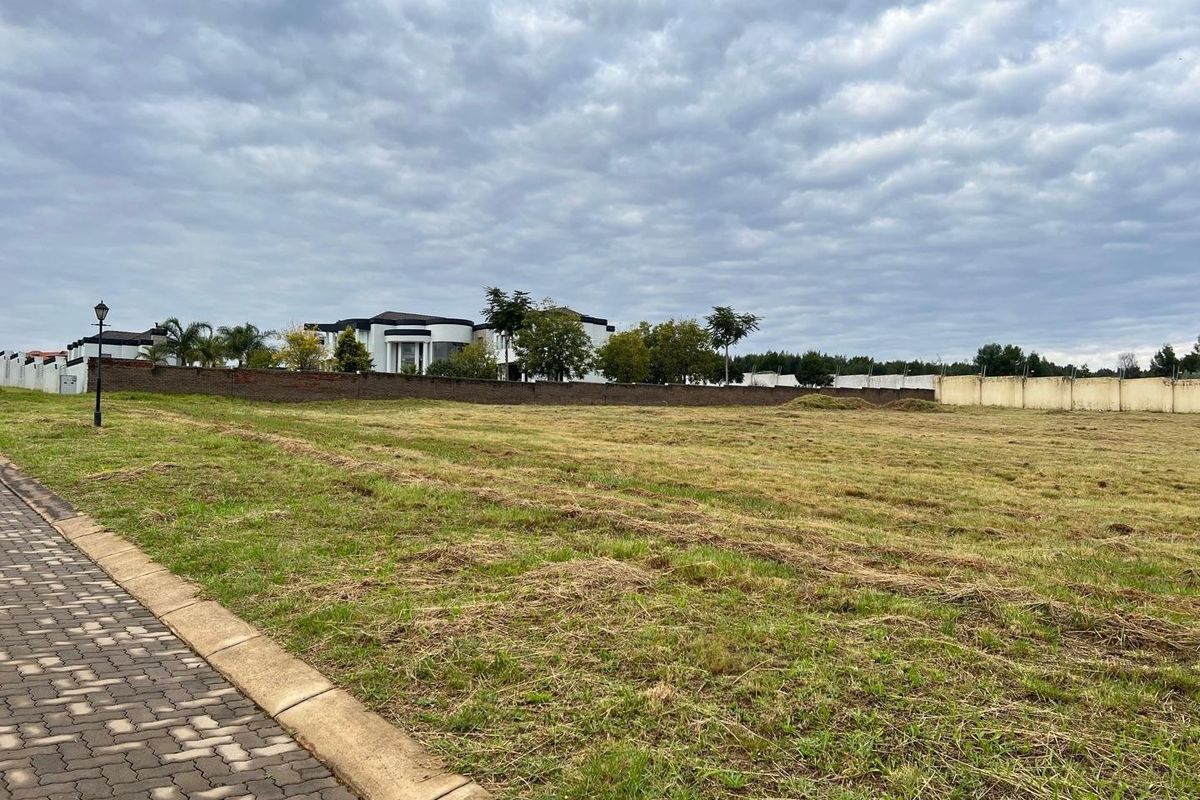 A vacant residential plot featuring a paved sidewalk, perimeter walling, and established neighborhood surroundings.