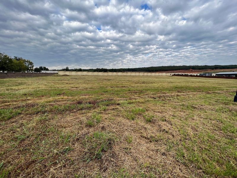 A wide-angle view of a vacant residential plot featuring open grass terrain and a perimeter boundary wall.