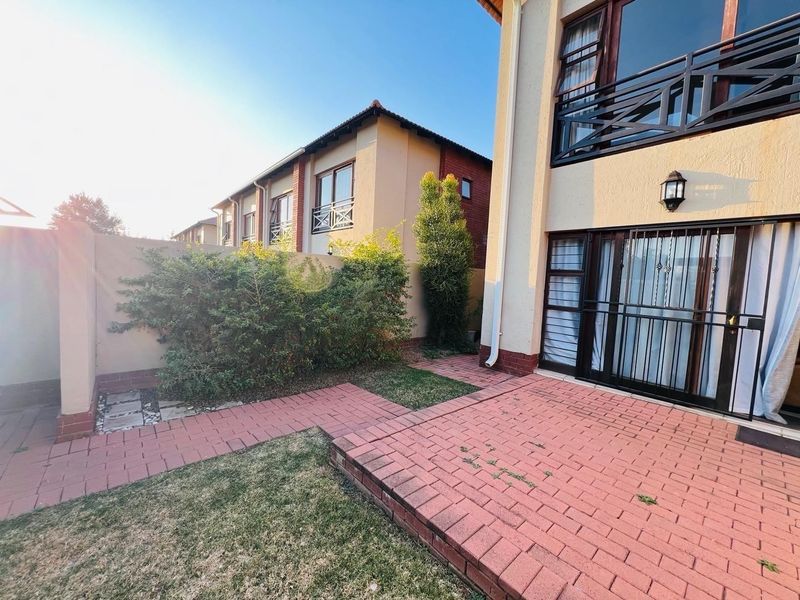 Rear view of the townhouse featuring a paved patio area, small garden, and access to the ground floor living space and upper balcony.