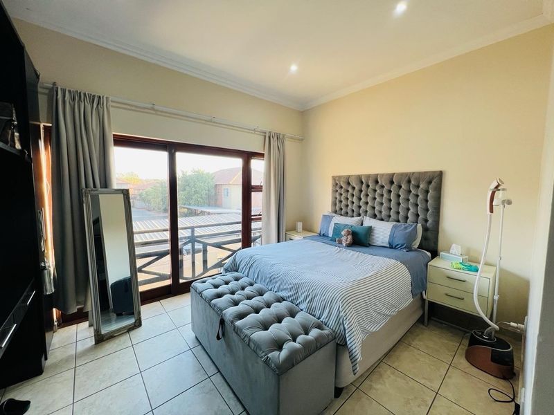 A well-lit bedroom featuring tiled flooring, coved ceilings, and a large sliding glass door providing access to an outdoor balcony area.