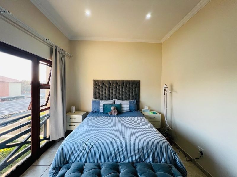 A well-lit bedroom featuring tiled flooring, recessed downlighting, and a sliding glass door providing access to an outdoor balcony area.