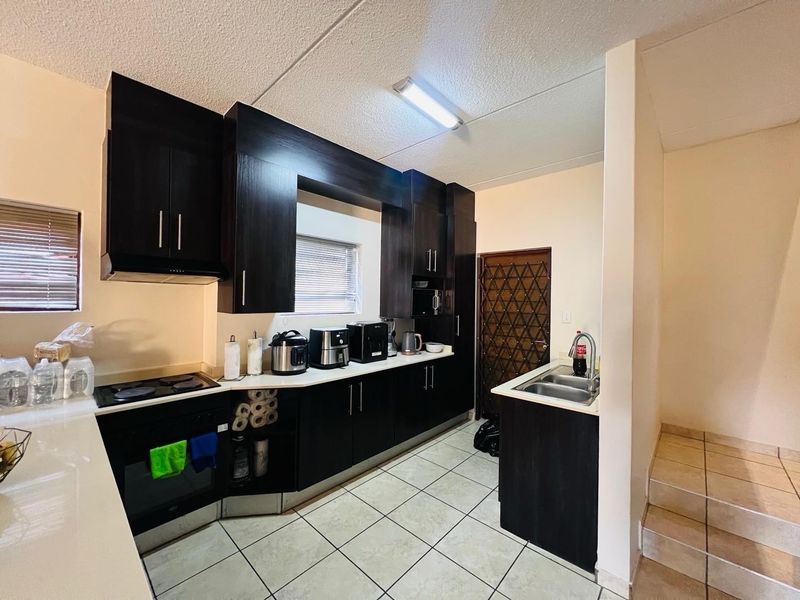 A functional kitchen featuring dark cabinetry, built-in oven and hob, double sink, and tiled flooring, with a security gate leading to the exterior.