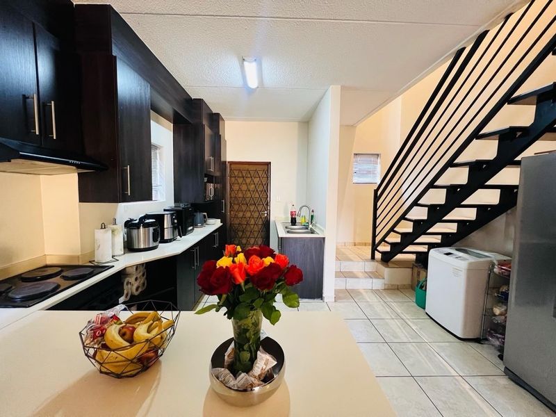 A functional kitchen featuring dark cabinetry, an electric hob, and tiled flooring, with an adjacent staircase leading to the upper level.