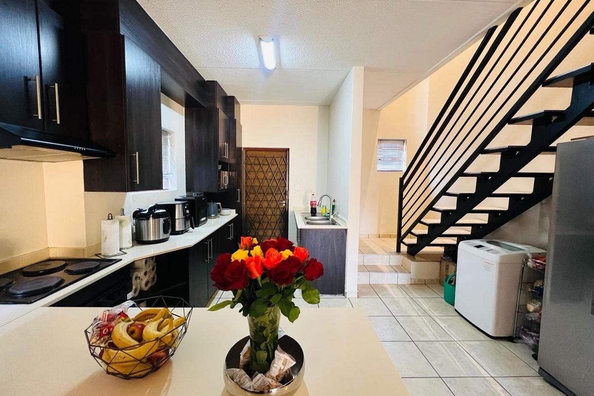 A functional kitchen featuring dark cabinetry, an electric hob, and tiled flooring, with an adjacent staircase leading to the upper level.