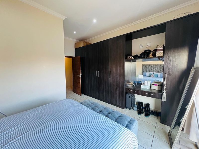 A bedroom featuring dark wood built-in cupboards with an integrated vanity area, tiled flooring, and recessed ceiling lighting.