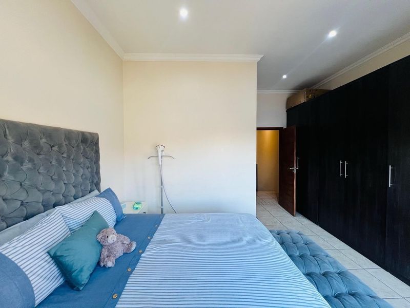 A well-maintained bedroom featuring built-in dark wood cupboards, tiled flooring, and recessed downlighting, offering a clean and functional living space.