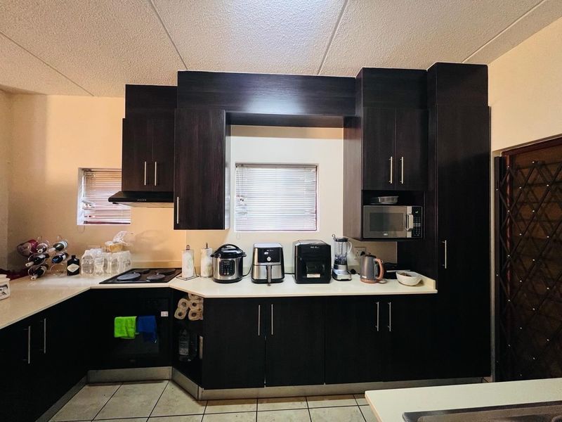 A functional kitchen featuring dark wood cabinetry, integrated appliances including an oven and hob, and tiled flooring with natural light from window blinds.