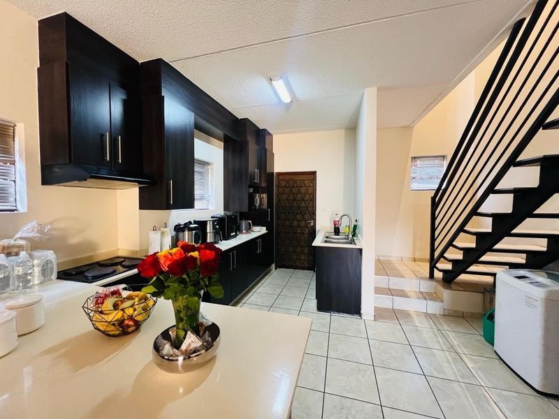 A functional kitchen featuring dark cabinetry, tiled flooring, and an integrated hob, adjacent to a staircase leading to the upper level.