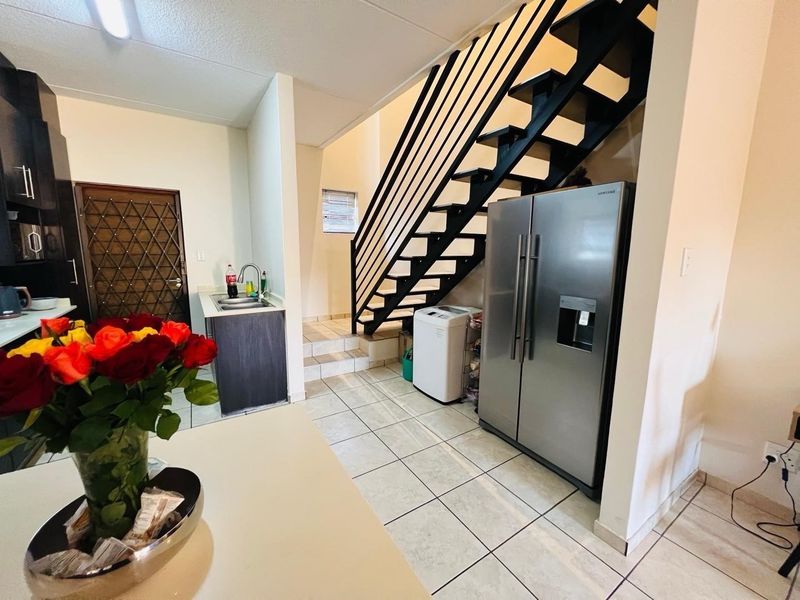 Open plan living area featuring a modern staircase, tiled flooring, and a functional kitchen corner with built-in cabinetry and sink.