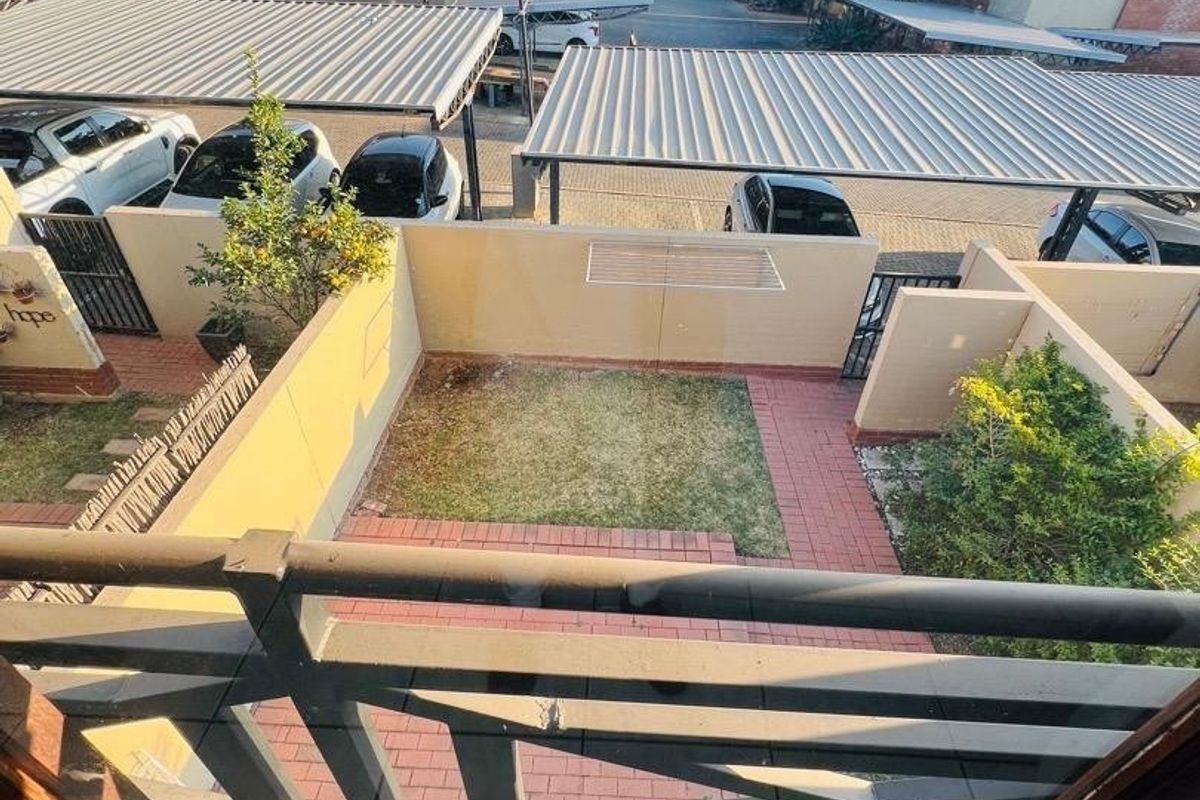 An elevated view of a private rear courtyard featuring a small lawn and paved area, overlooking a complex parking area with metal carports.