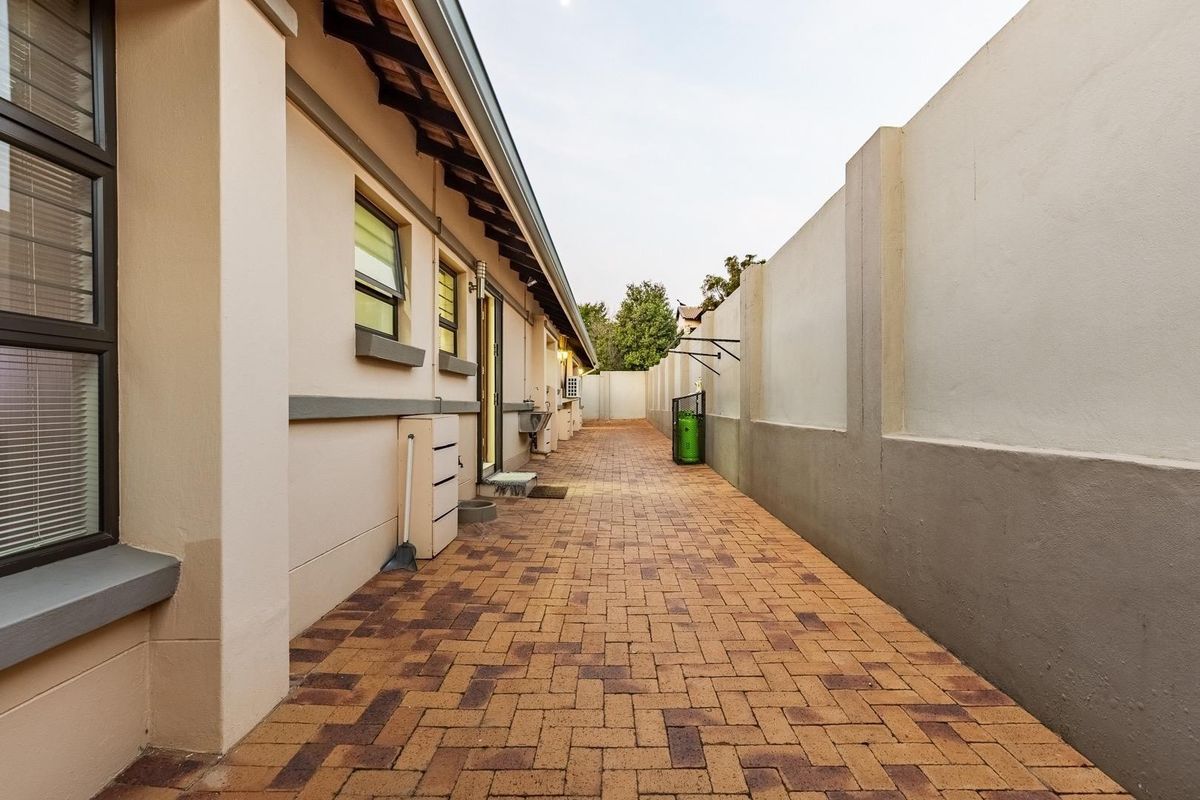 A clean and well-maintained paved side passage or rear exterior walkway featuring high boundary walls and external utility access.