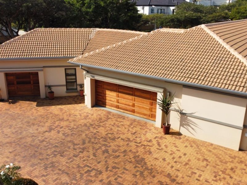 Aerial view of the property frontage featuring a large brick-paved driveway, multiple wooden garage doors, and a well-maintained tiled roof.
