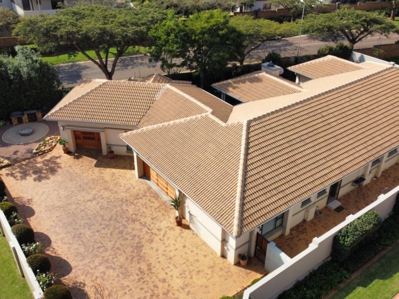Aerial view of a residential property featuring a tiled roof, paved driveway, and garage access within a secure boundary wall.