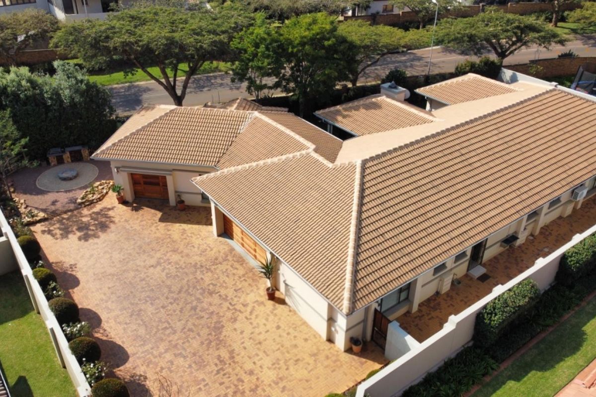 Aerial view of a residential property featuring a tiled roof, paved driveway, and garage access within a secure boundary wall.