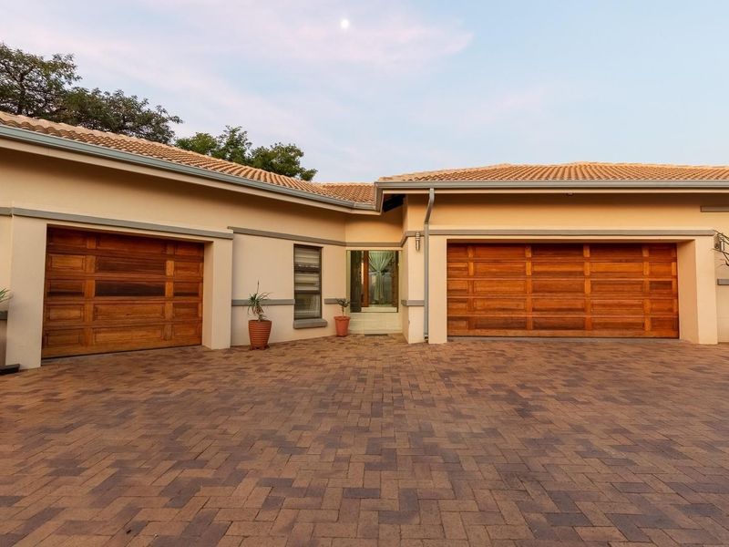 Front elevation of a residential property featuring a paved driveway, two wooden garage doors, and a tiled roof.