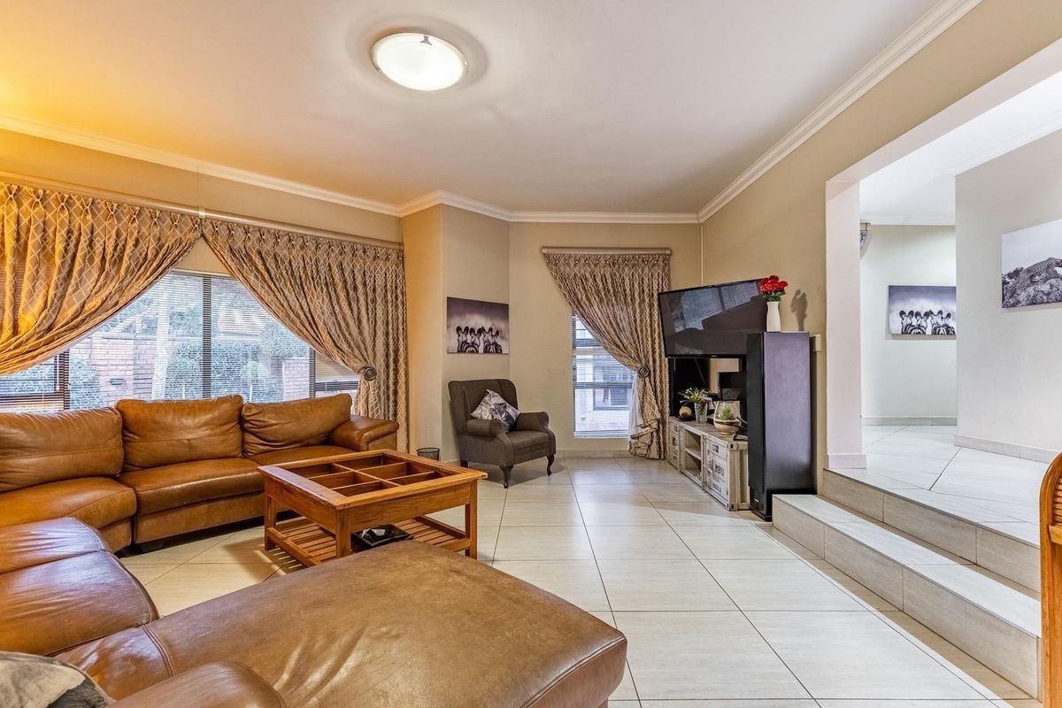 Spacious living room featuring large windows, tiled flooring, and a raised floor transition leading to an adjacent hallway area.