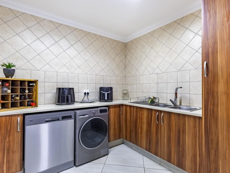 A functional laundry room featuring built-in wood-finish cabinetry, laminate countertops, a double stainless steel sink, and tiled backsplash.