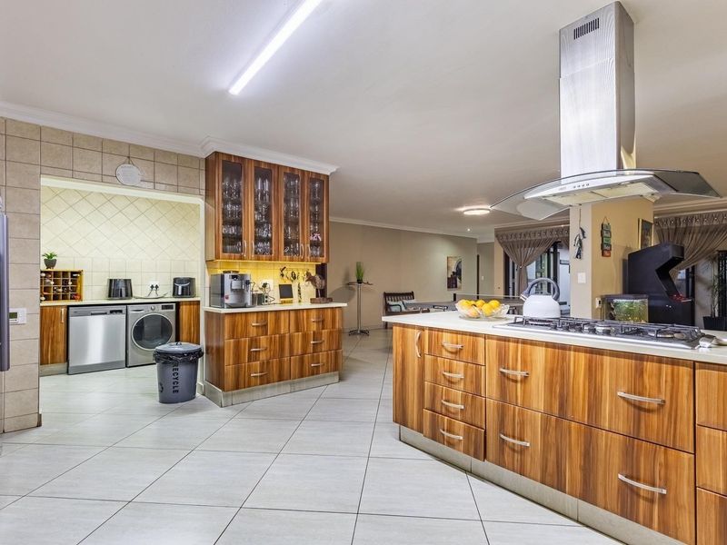 Spacious open-plan kitchen featuring a central island with gas hob, extractor fan, and extensive wooden cabinetry, seamlessly flowing into the adjacent living area.