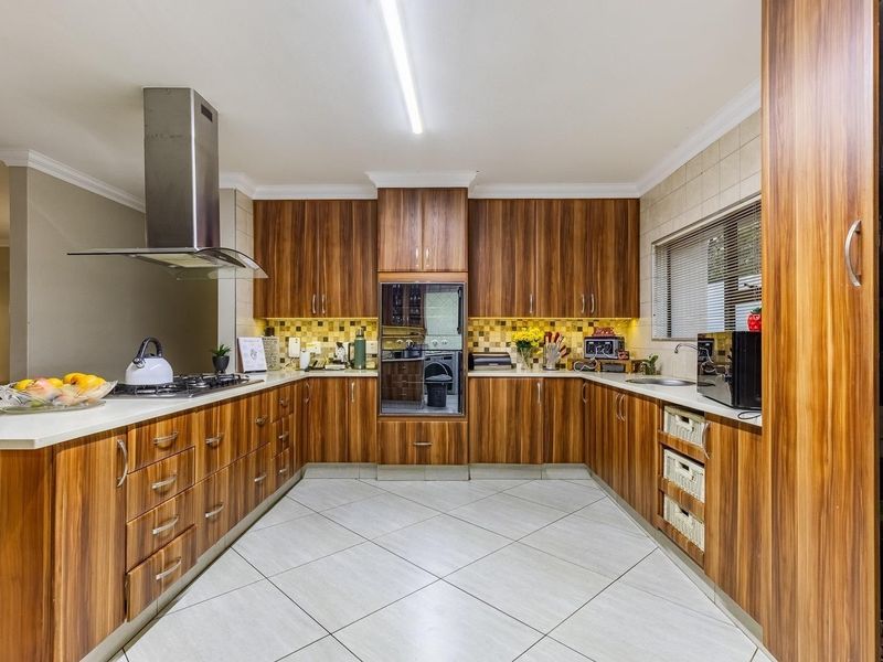 A well-maintained kitchen featuring wood-grain cabinetry, a stainless steel extractor fan, gas hob, built-in oven, and tiled flooring with ample counter space.