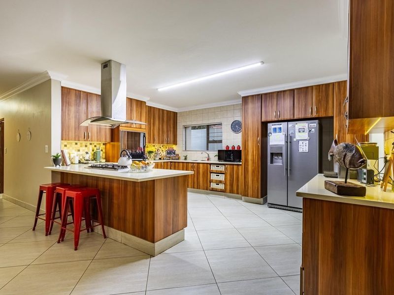 Spacious modern kitchen featuring wood veneer cabinetry, stone countertops, a central island with a gas hob, and high-quality stainless steel appliances.