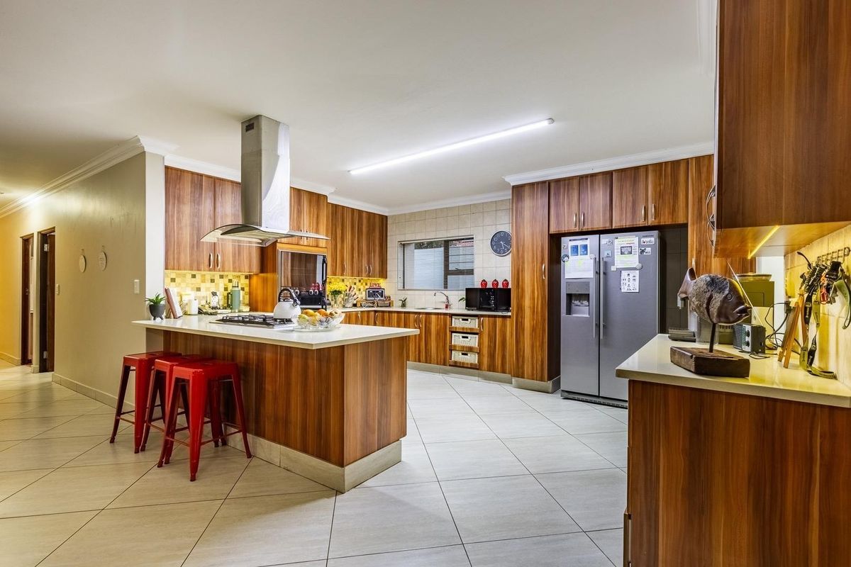 Spacious modern kitchen featuring wood veneer cabinetry, stone countertops, a central island with a gas hob, and high-quality stainless steel appliances.
