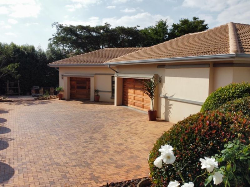 A well-maintained front exterior featuring a spacious brick-paved driveway leading to a double garage with wooden doors and a neat landscaped garden.