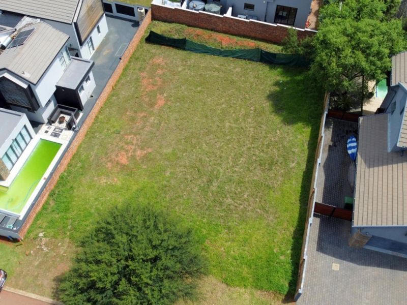 Aerial view of a vacant residential plot situated between existing developed properties, featuring a level grass lawn and perimeter boundary walls.