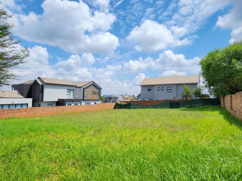 A vacant residential plot featuring a grassed surface enclosed by perimeter brick walls and temporary shade cloth fencing in a developed estate.