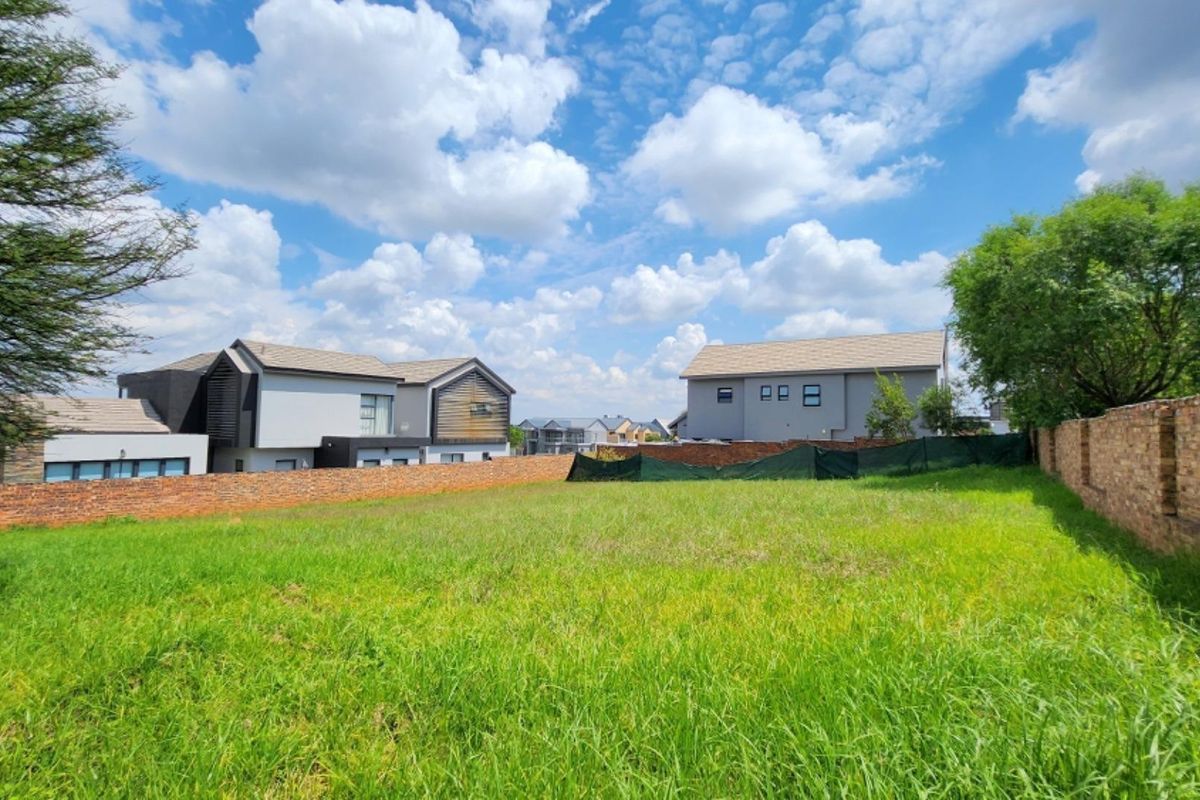 A vacant residential plot featuring a grassed surface enclosed by perimeter brick walls and temporary shade cloth fencing in a developed estate.