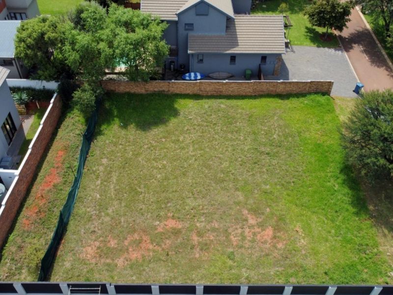An aerial view of a vacant residential plot featuring a grass lawn, enclosed by boundary walls and fencing in a developed neighborhood.
